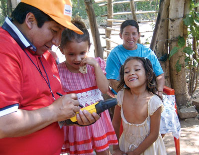 World vision worker enters data on the GPS unit while children watch